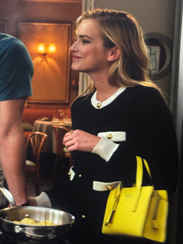 Woman wearing black and white sweater with gold buttons, and holding yellow purse.