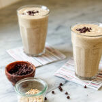 Two healthy date protein shakes are served in clear glasses on colorful napkins.