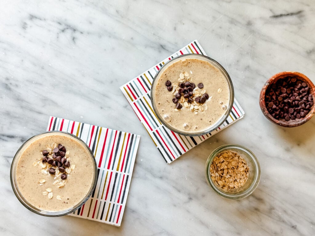 Healthy date protein shakes are served in two clear glasses and topped with oats and mini chocolate chips.