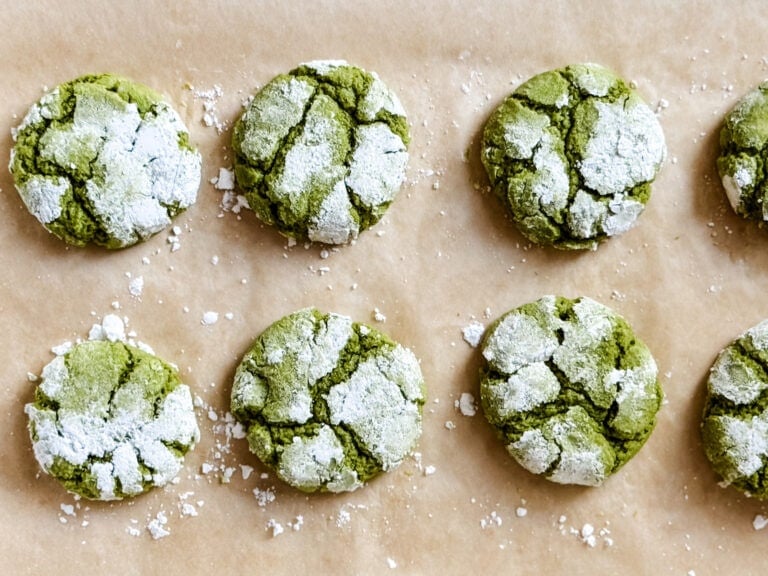 Matcha crinkle cookies are on a parchment paper-lined baking sheet fresh out of the oven.