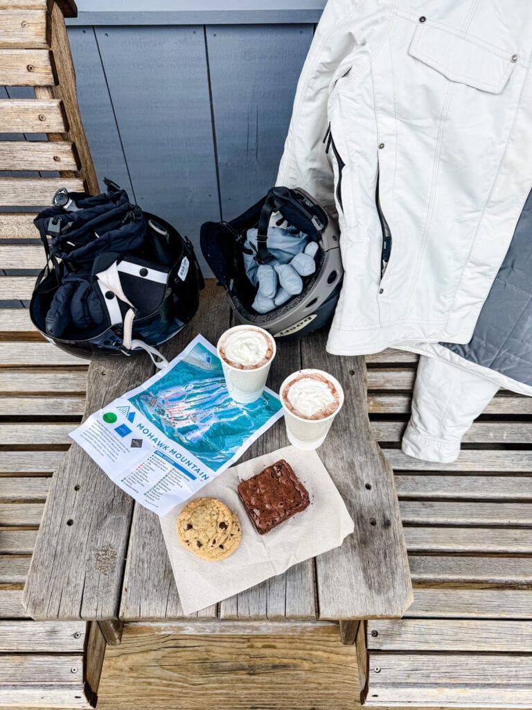 Two cups of hot chocolate along with chocolate chip cookies and a brownie are on table on the deck of the lodge at Mohawk Mountain.