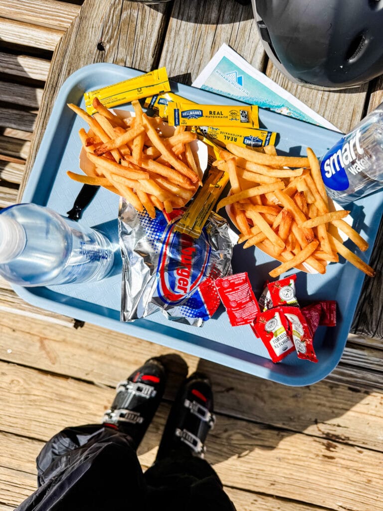 A hamburger, French fries and two bottles of water are on a tray outside the lodge and on the deck.