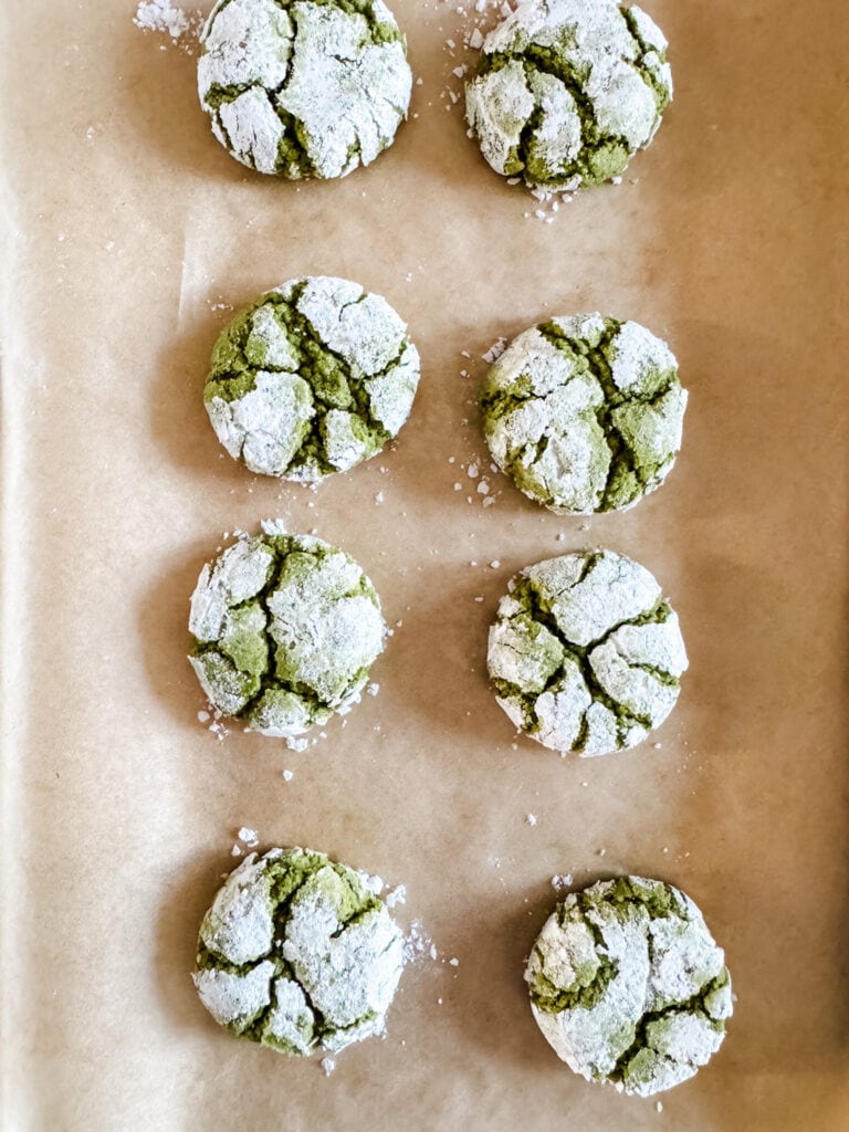 Matcha crinkle cookies on parchment paper are fresh from the oven.