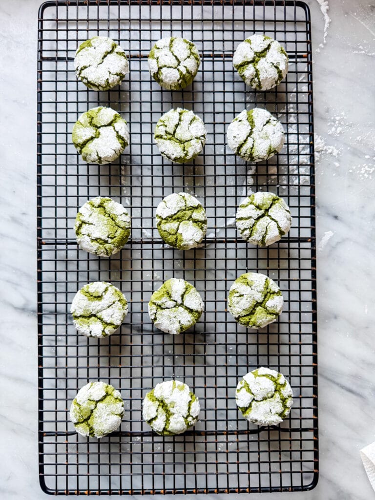 Green matcha crinkle cookies are cooling on a wire rack.