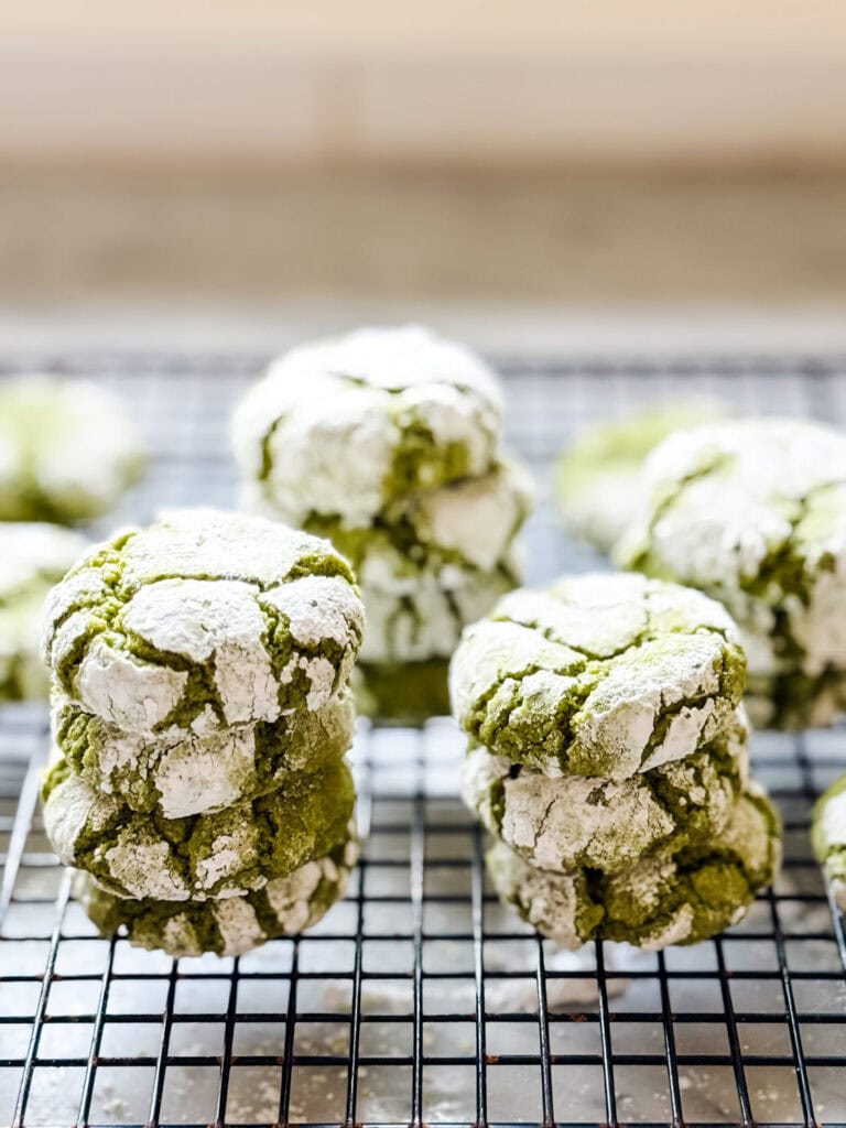 Matcha crinkle cookies are stacked on a wire cooling rack.