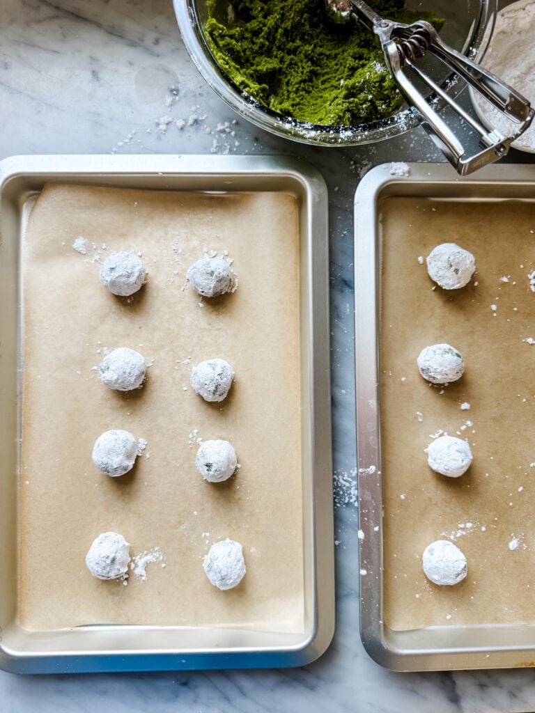 Rolled cookie dough balls are placed on a parchment paper lined baking sheet.