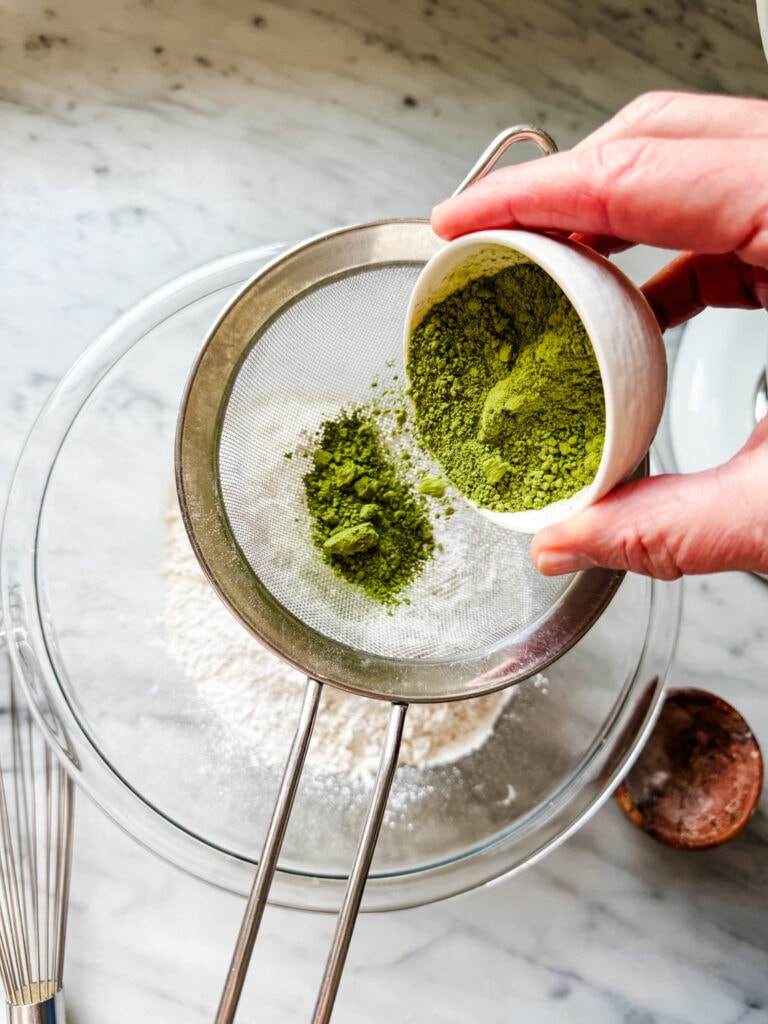 Sifting matched powder into the flour mixture is a step in making matcha crinkle cookies.