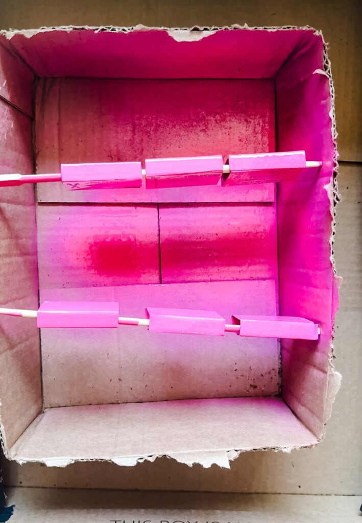 Matchbooks on chopsticks inside a larger box to spraypaint pink.