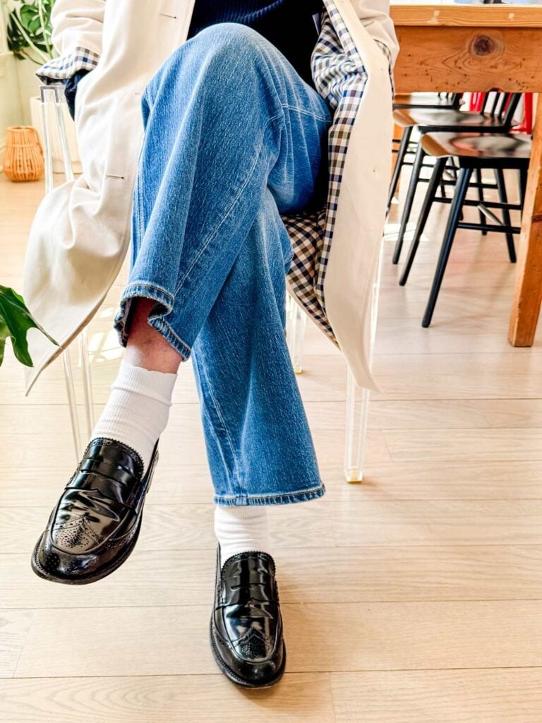 A woman wearing jeans, white socks, and loafers is sitting in a Ghost Chair.