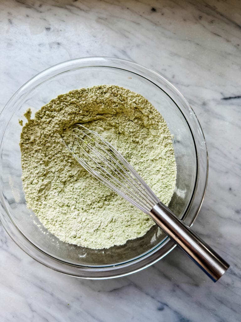 Flour, matcha powder, baking soda, baking powder, and salt are mixed in a glass bowl.