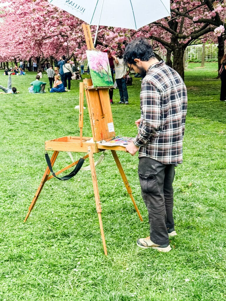 An artist is painting the cherry blossoms at the Brooklyn Botanic Garden.