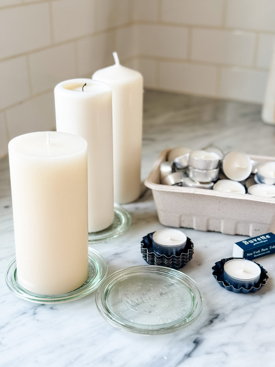 Tea lights in mini tart tins and pillar candles on glass Weck jar saucers for setting a table for a French dinner party.