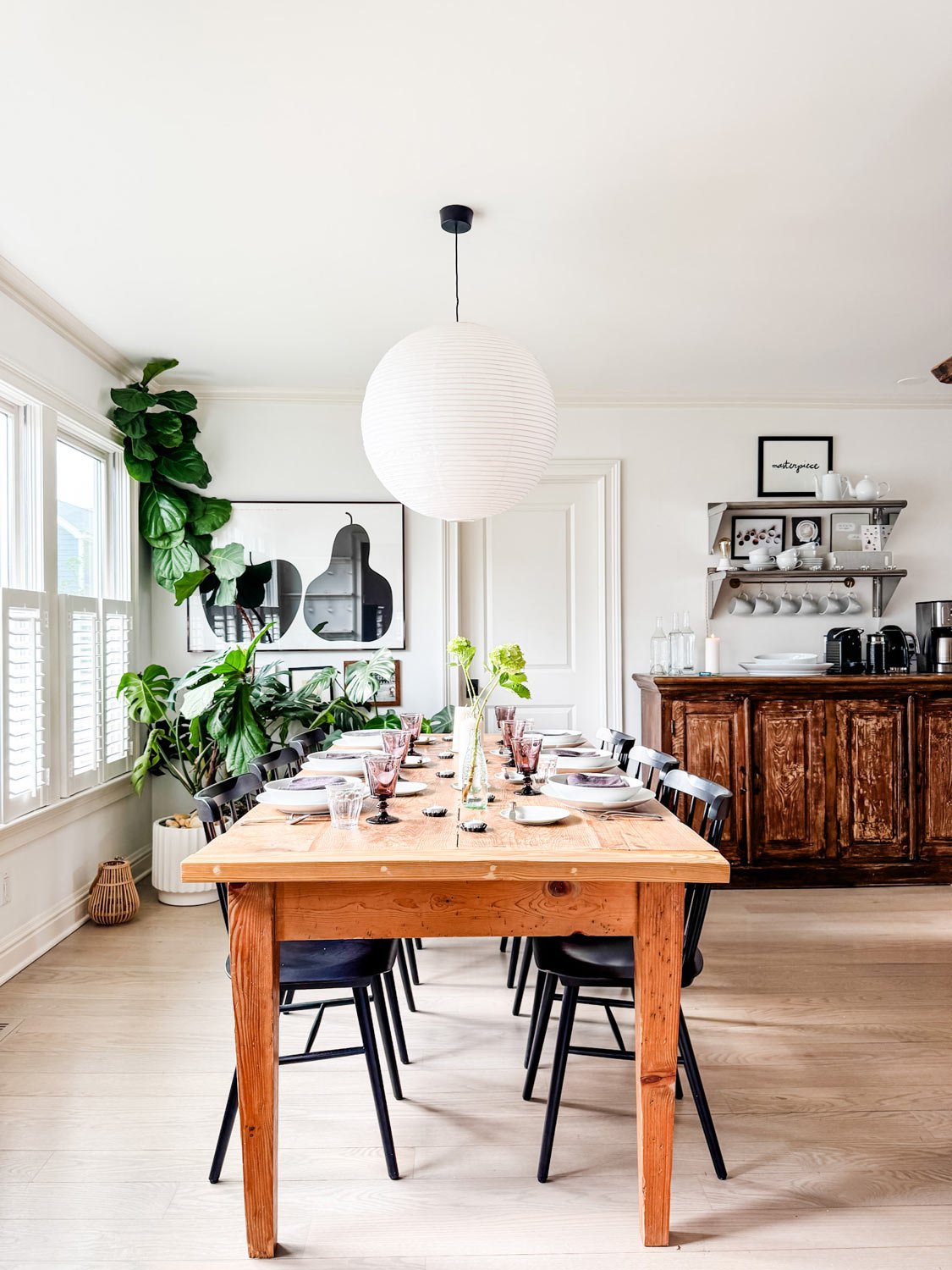 A French style dinner party table set with whote dishes, flowers in bottles, candles, mmix of glassware.