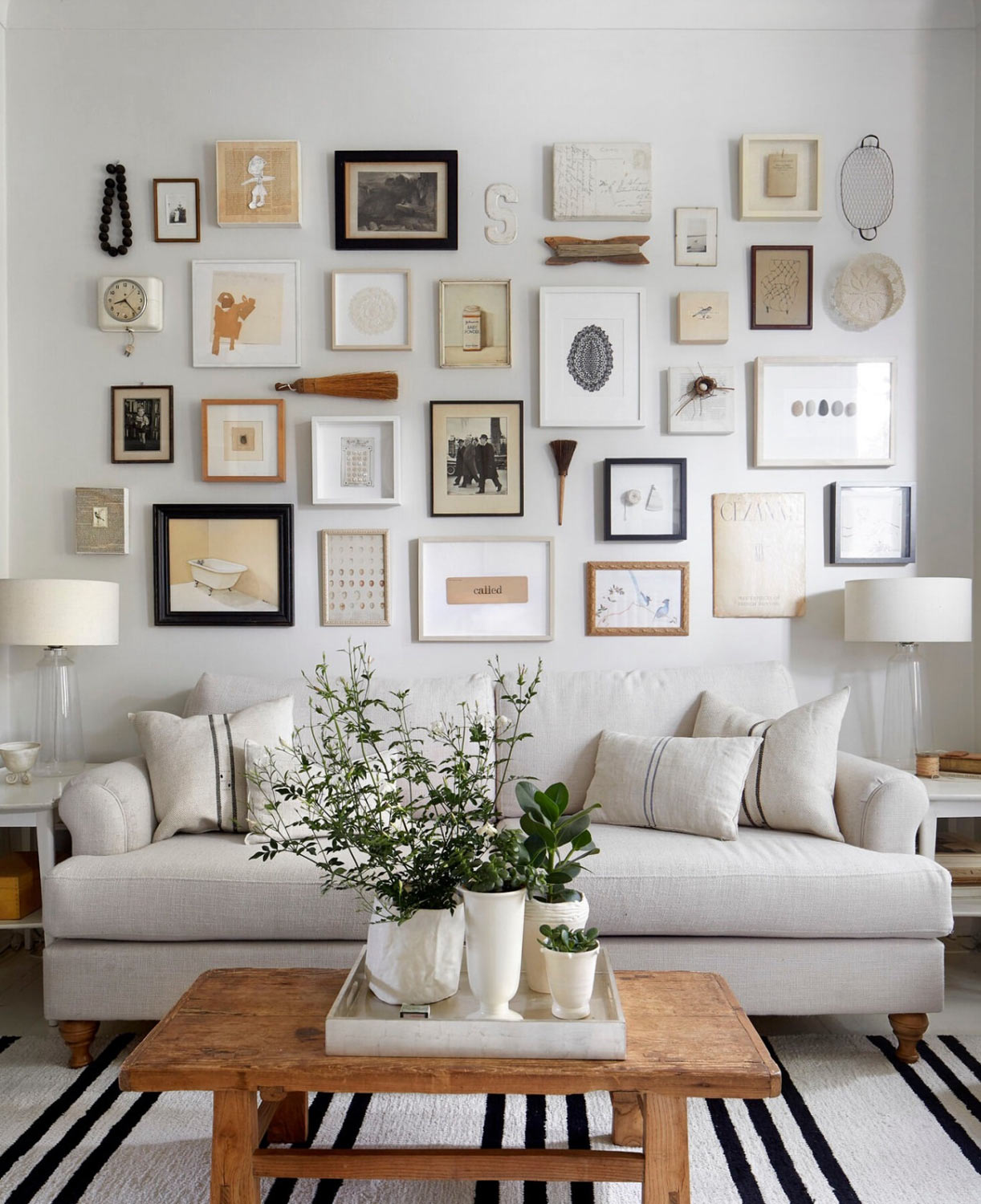 White sofa with gallery wall, coffee table with tray and grouping of white vases with plants and greenery.