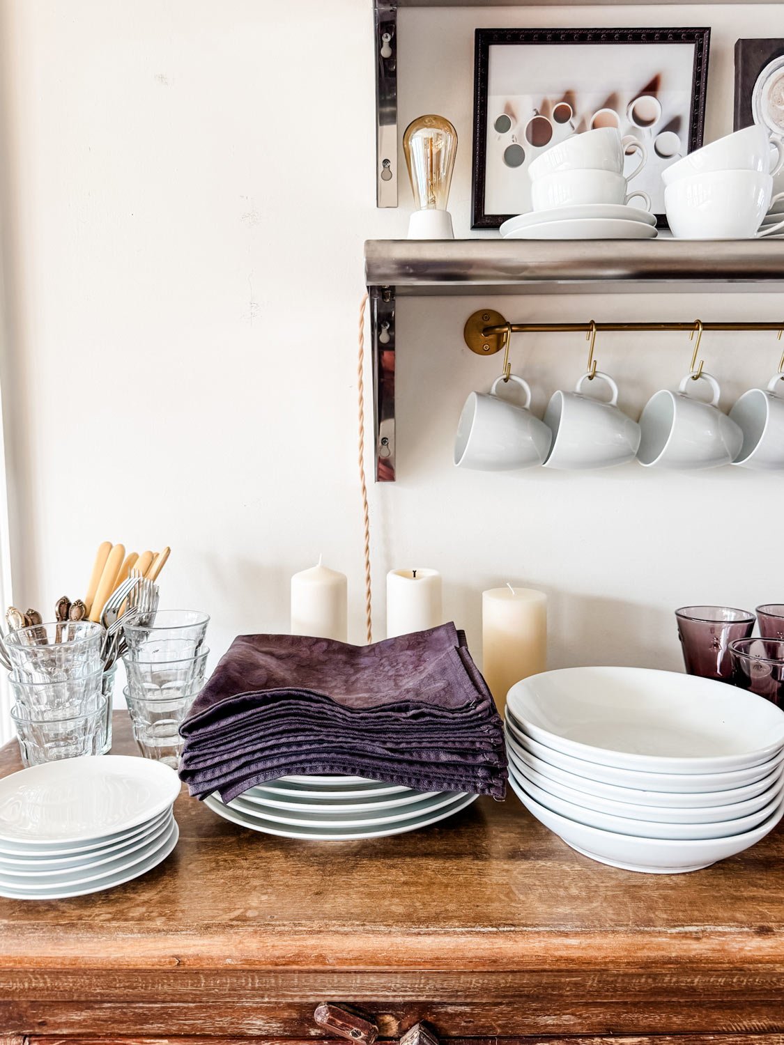 Mix of flatware for a Frnech finner party in a working glass nbext to Duralex glasses, tea lights, bowls, napkins on stacked plates.