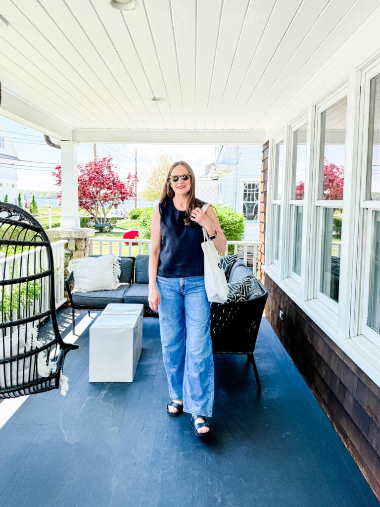 Woman wearing jeans, black tank, tote bag on porch.