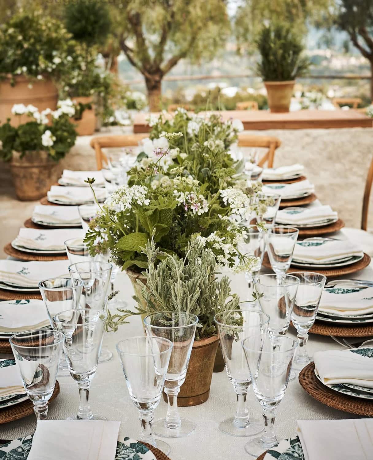 Table with clear glasses, plates, napkins, potted pants.