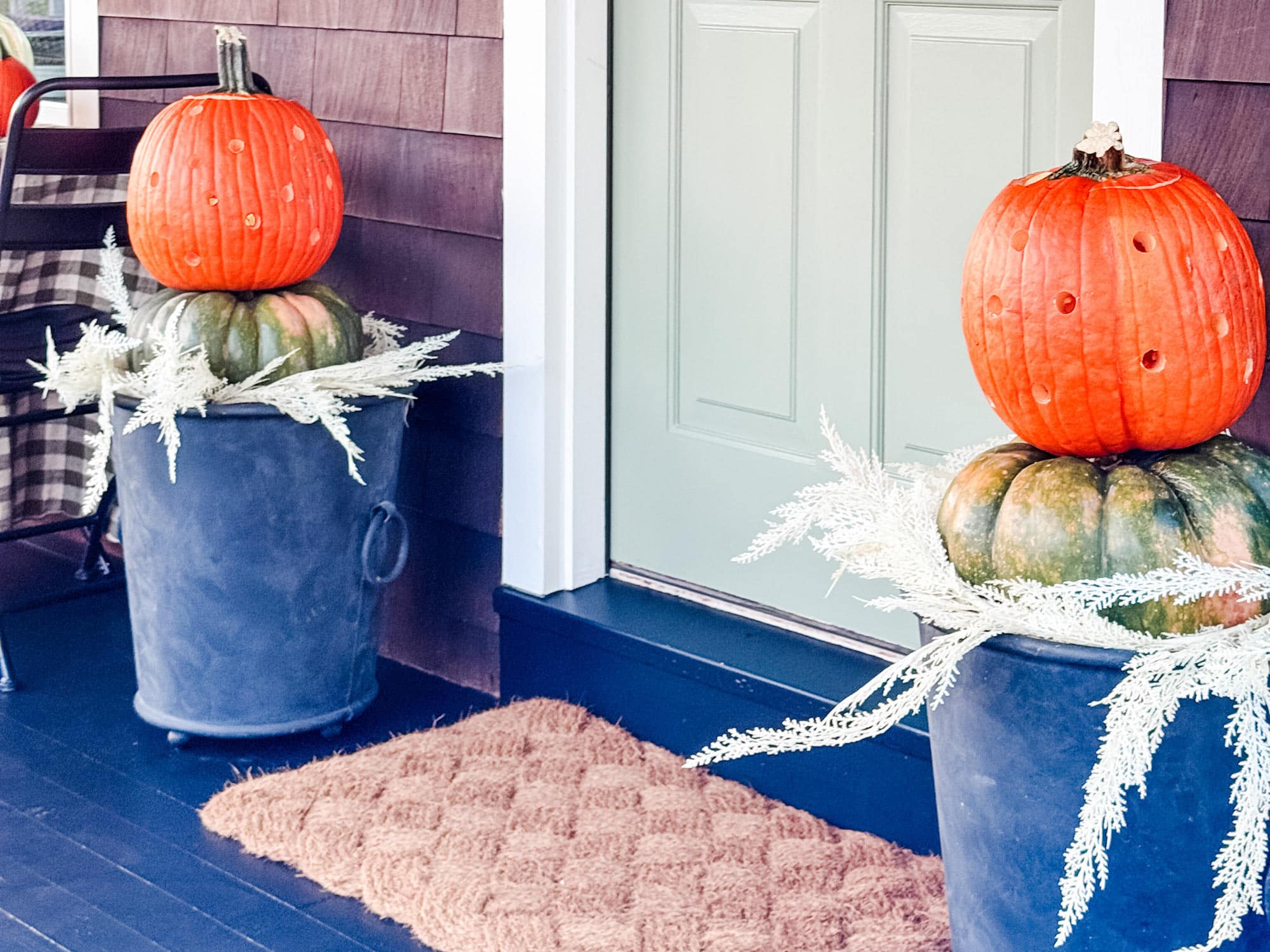 Pumpkins stacked in planters by green door.