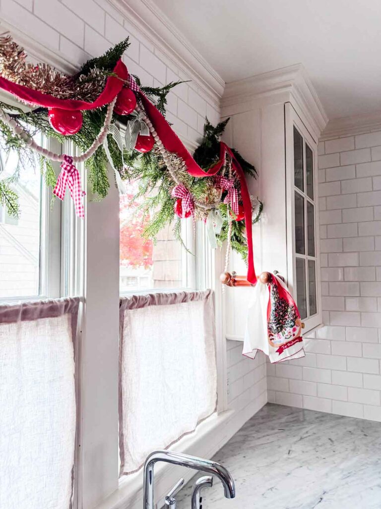 Ralph Lauren Christmas garland made from old shirts that are checked and striped with other garlands above a farm sink with windows that have cafe curtains.