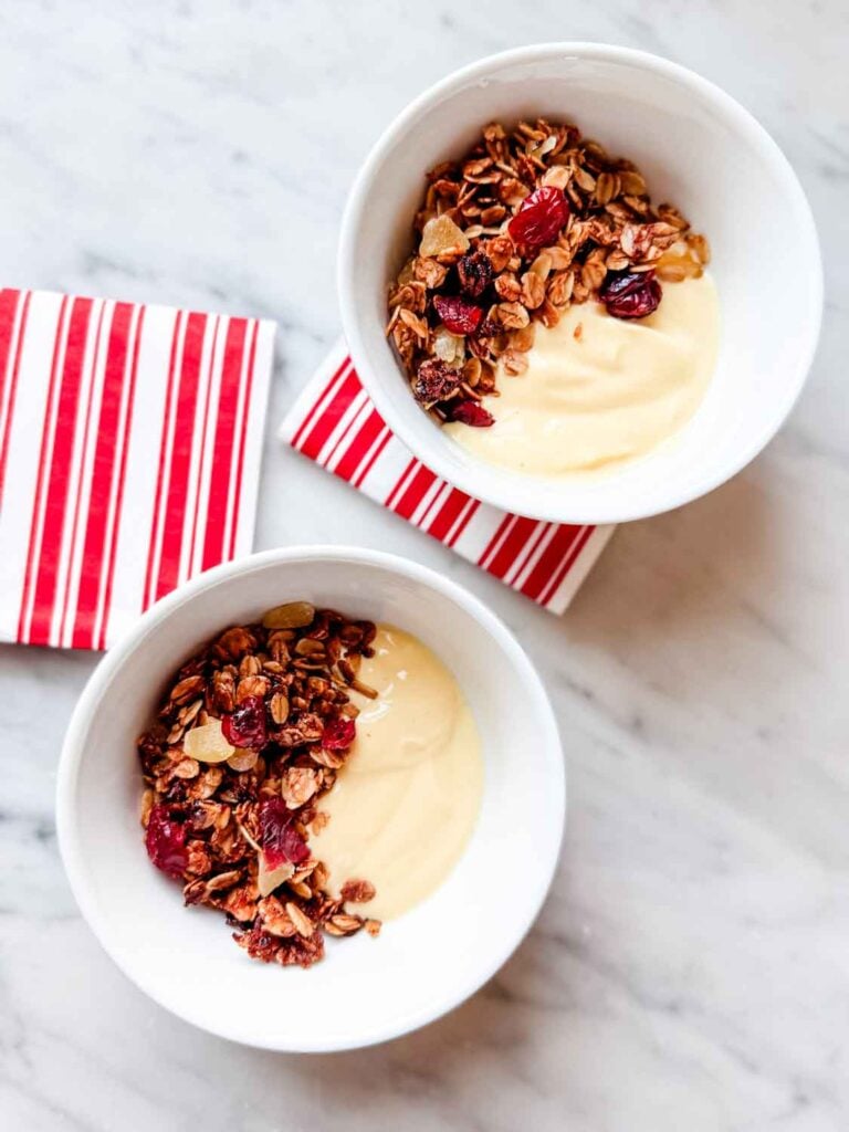Gingerbread granola with eggnog yogurt in small whote bowls with red and white stripe napkins.