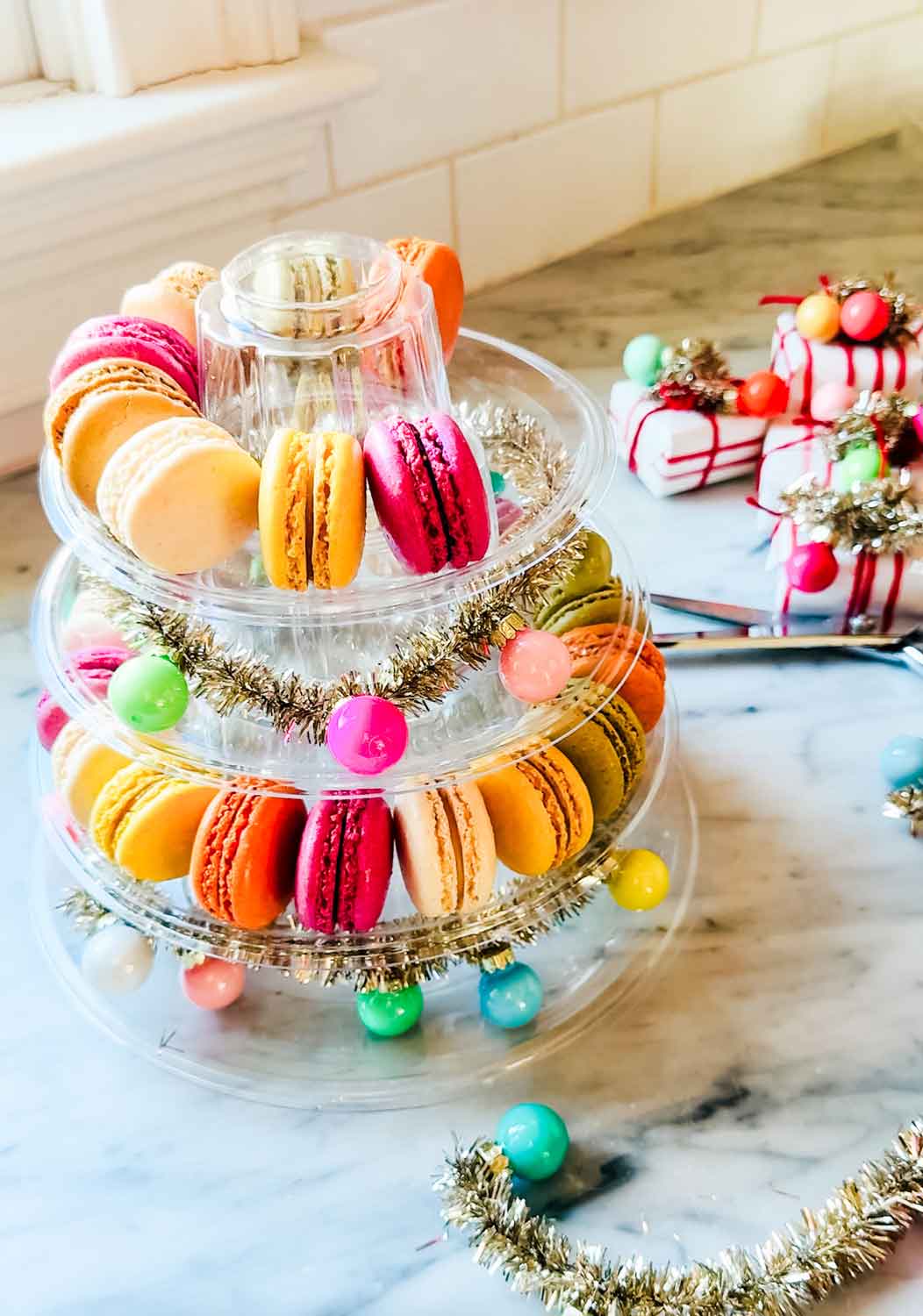 Colorful macarons on marble countertop, clear macaron tower, tinsel garland.