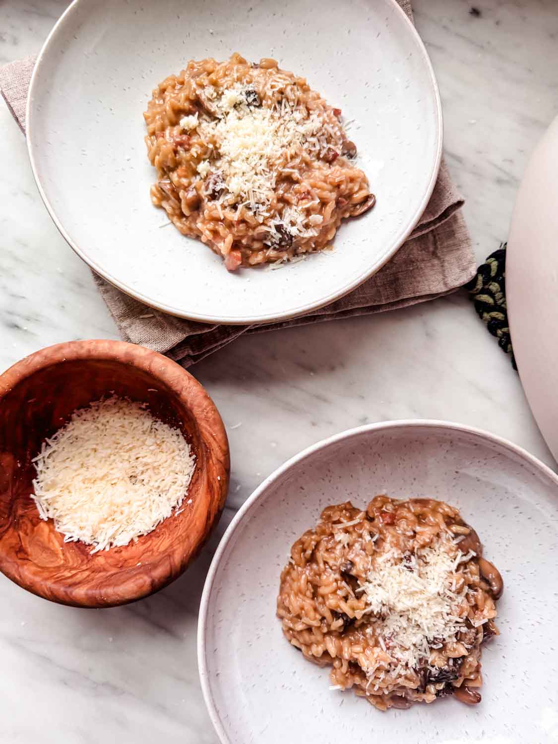 Two bowls of risotto topped with parmesan cheese are sitting next to a wooden bowl with grated cheese.