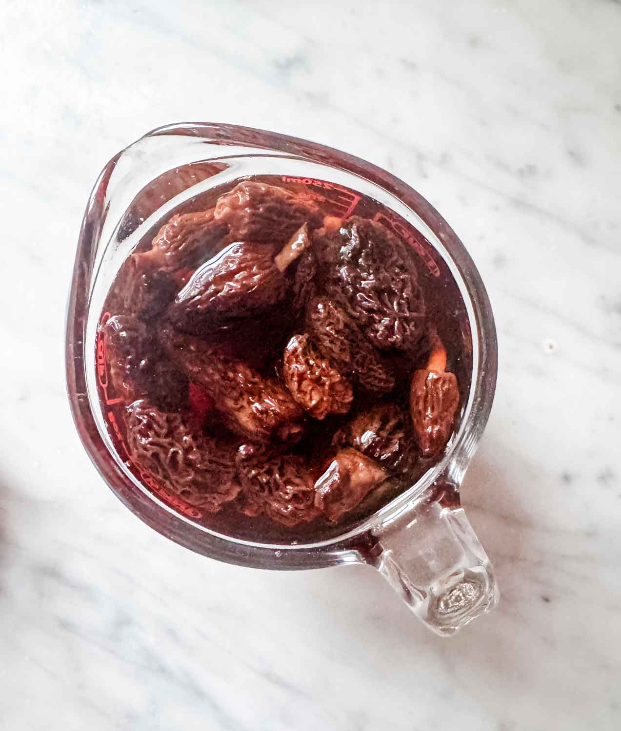 Dried morel mushrooms with boiling water are in glass measuring cup.