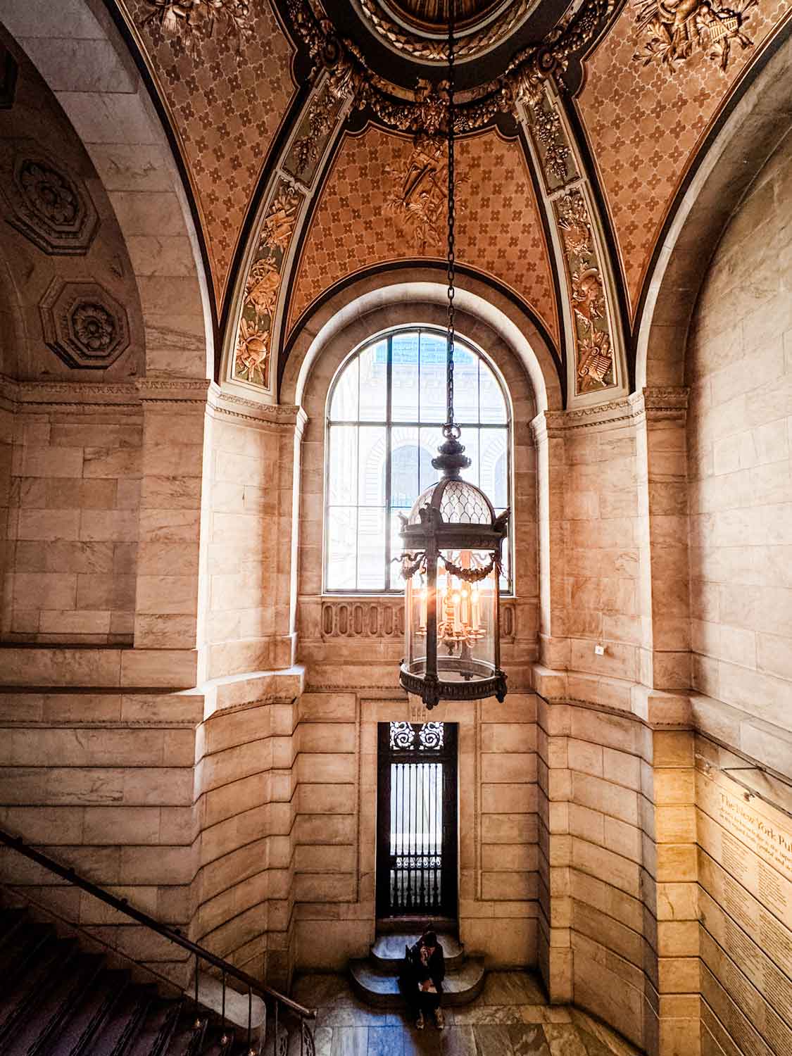 A large glass chandelier hangs above the landing between the first and second floors of the NYPL.