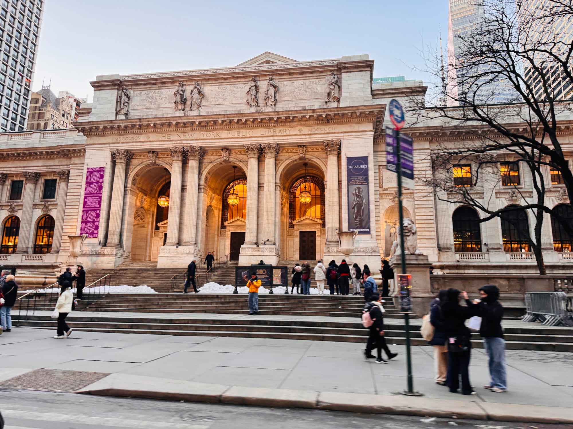 The outside of the New York Public Library at the end of the day, with people walking by.