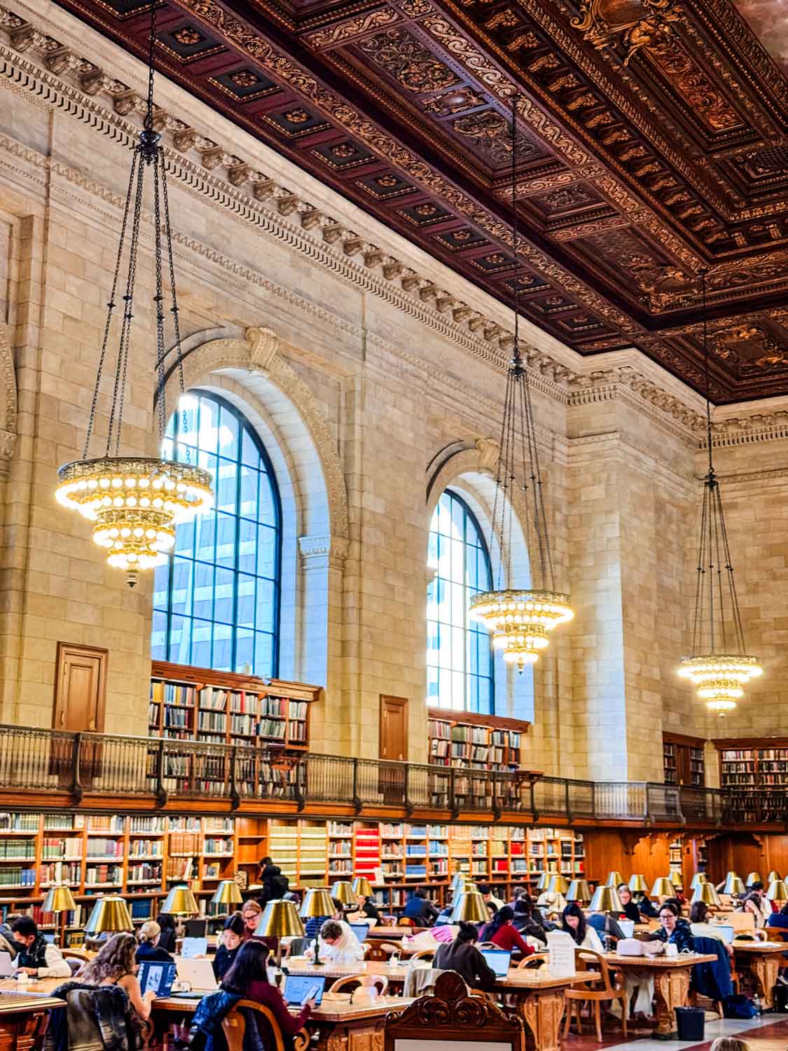 The Rose Reading Room is lined with book shelves, oak tables with lamps, and people quiet working.