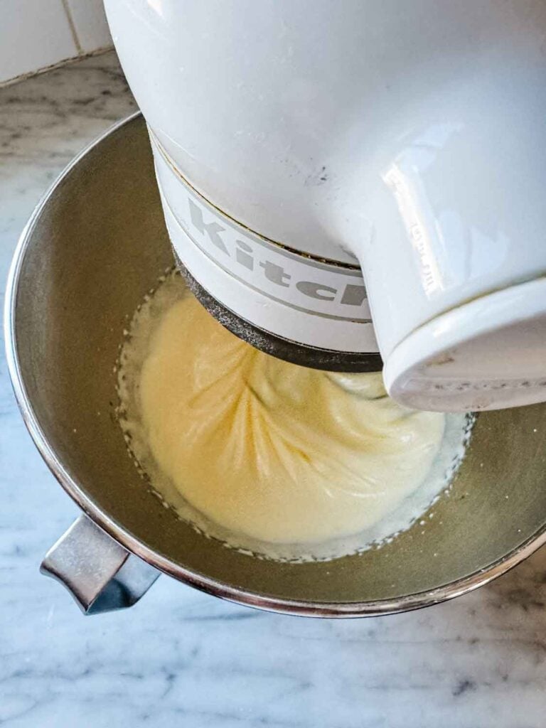 Eggs and sugar are being beaten in a white stand mixer with a stainless steel bowl.