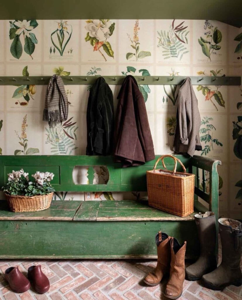 In this Hudson Valley house the mud room has an old green wooden bench with a coat rack running the length of the wall. On the brick floor are various shoes and boots.