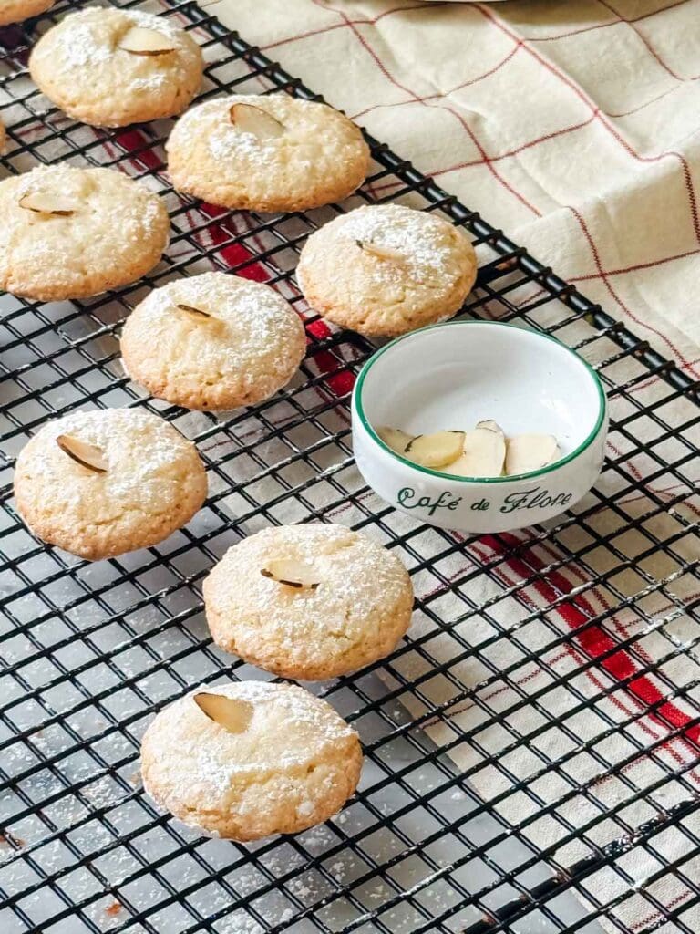 Saint-Émilion macarons with slivered almonds are baked and cooling on a wire rack.