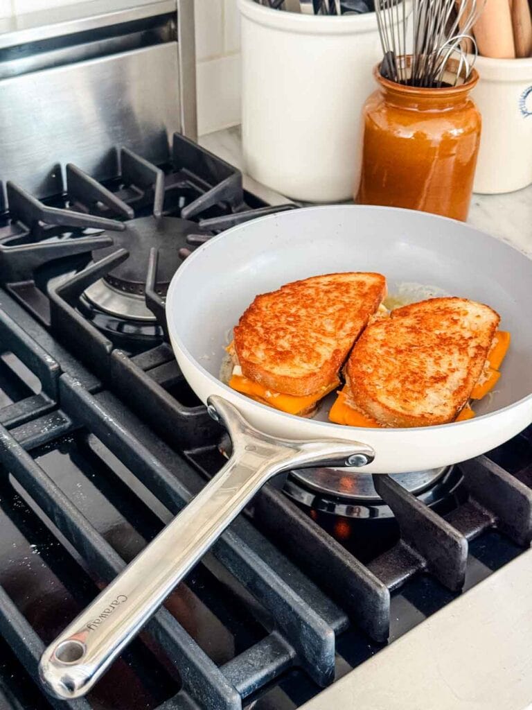 Two tuna melts are toasted in a non-stick skillet on a gas-powered stove.