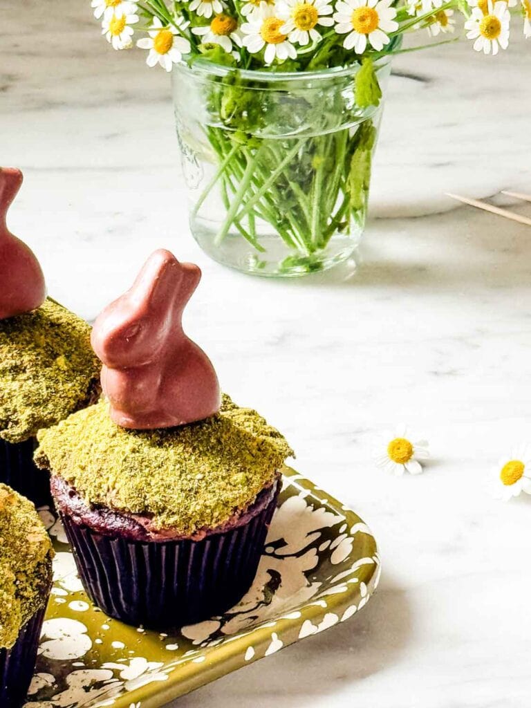 Chocolate cupcakes with matcha moss, chocolate bunnies on green splatter tray. Chamomile flowers.