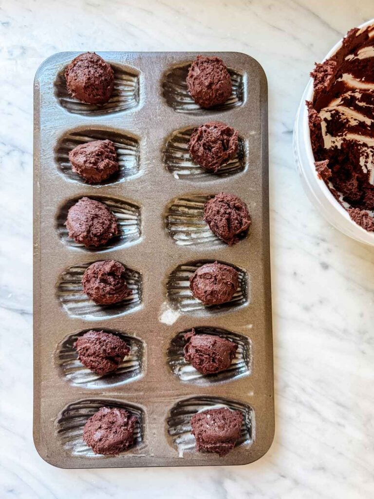 Balls of cookie dough are placed in the center of each mold on a Madeleine baking sheet and are ready to be baked in the oven.