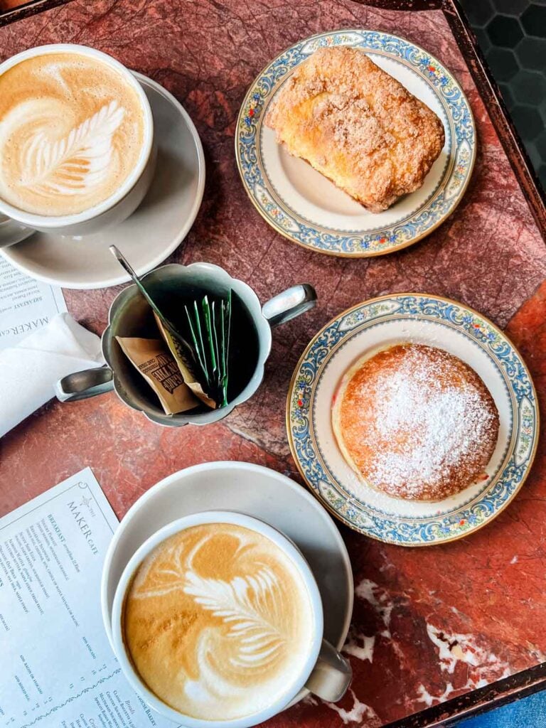 Coffee, small floral rimmed plates with pastries and sugar bowl with packets, menu, on red marble tabletop.