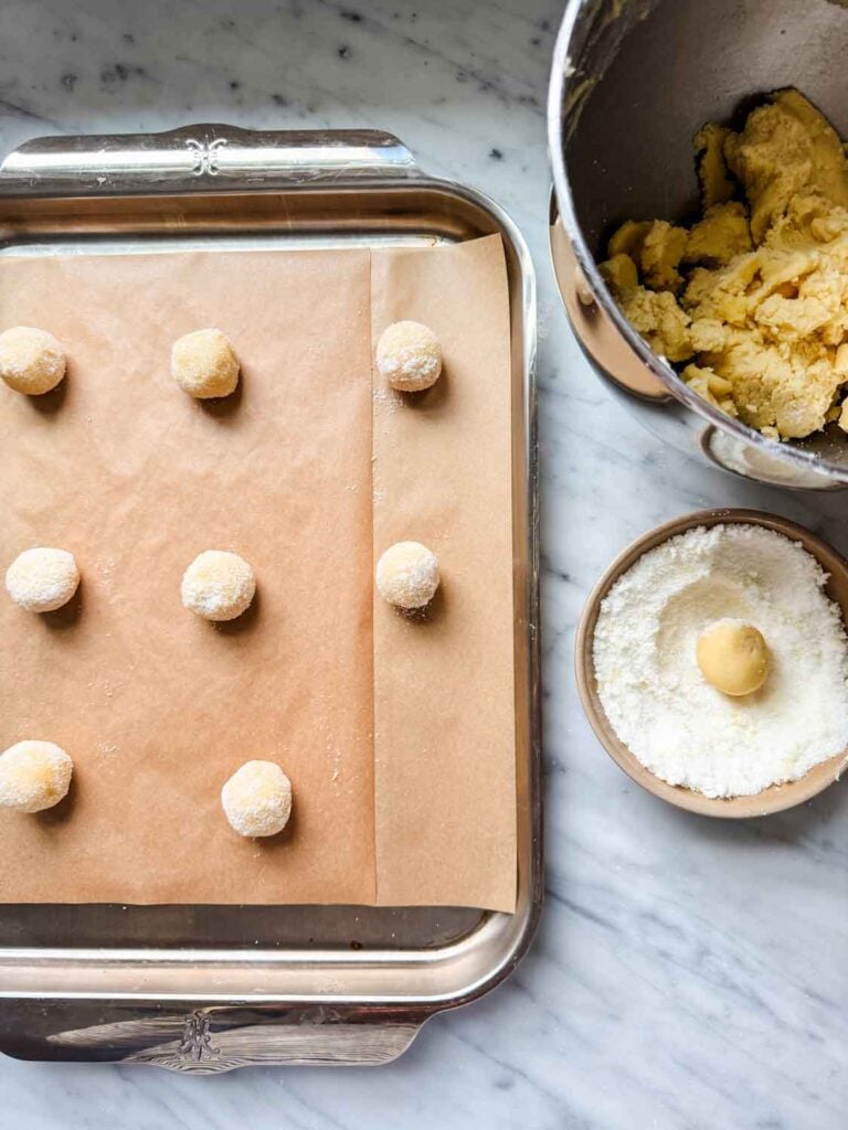 Cookie dough has been formed into balls, rolled in granulated sugar, and placed on a parchment paper-lined baking sheet.