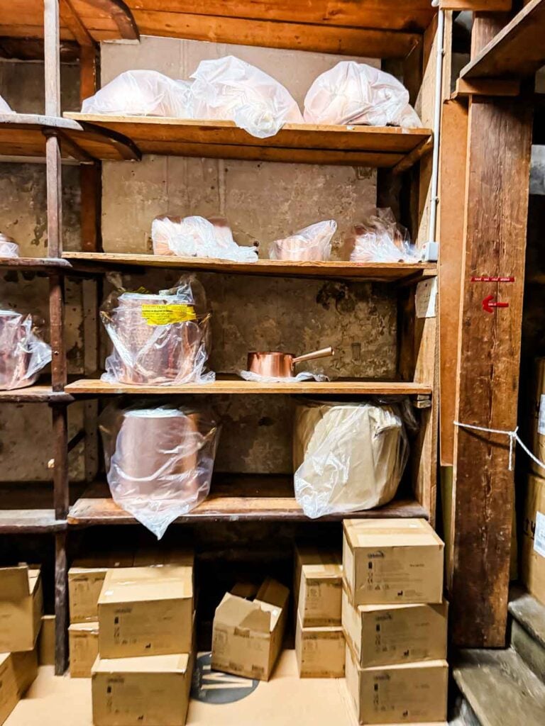 Copper pots covered in plastic and inside boxes line the floor and wooden shelves in this kitchen supply store in Paris.