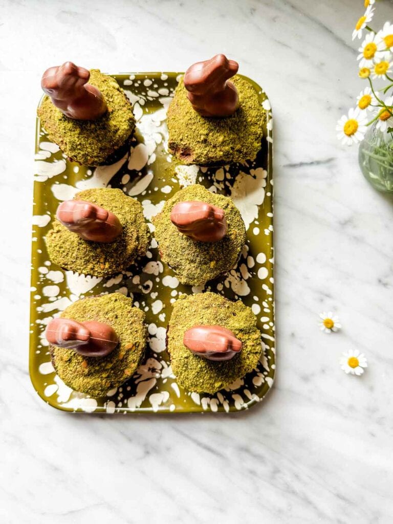 Chocolate cupcakes with matcha moss, chocolate bunnies on green splatter tray. Chamomile flowers.