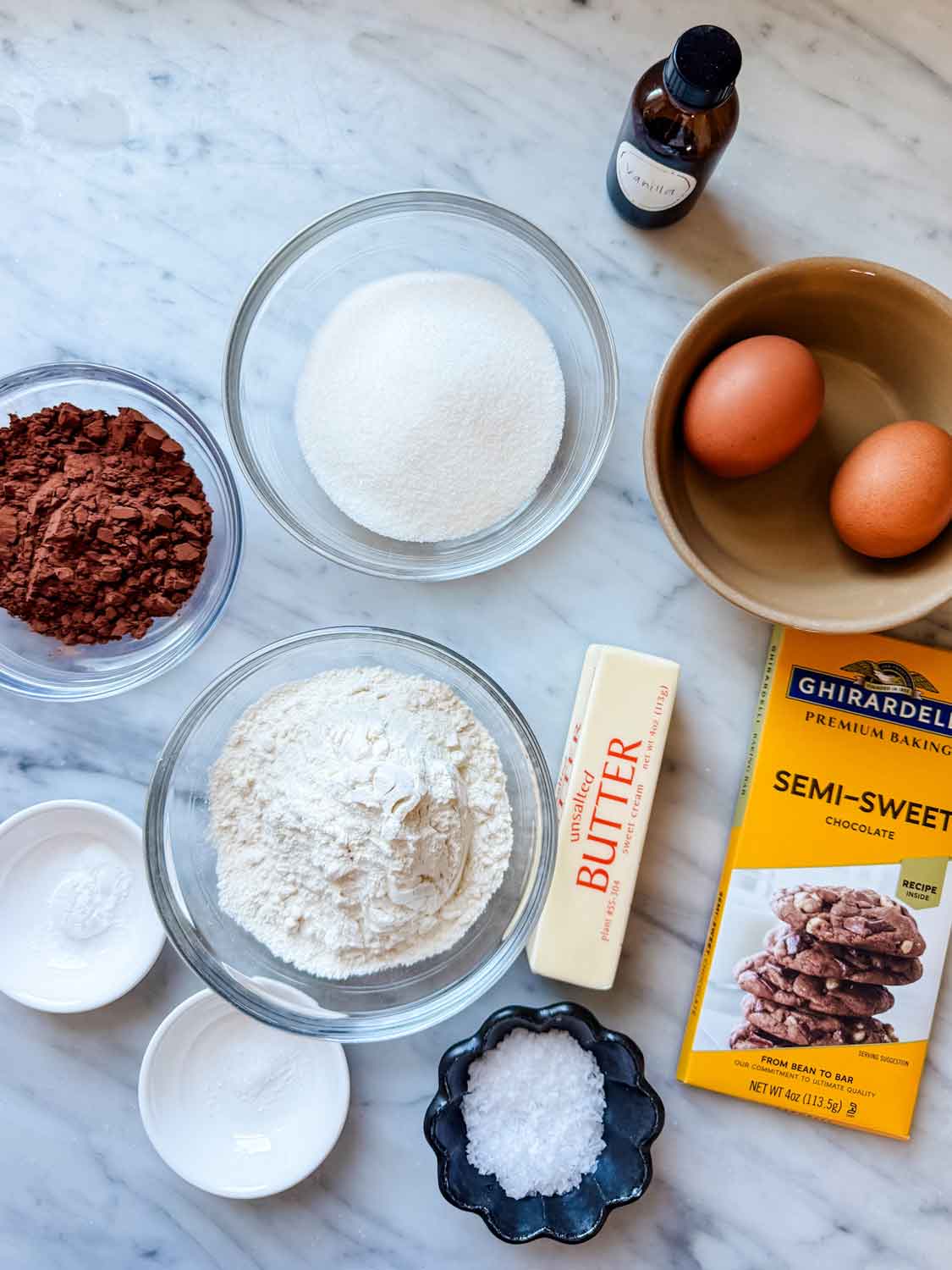 All the ingredients for making double dark chocolate madeleines are measured, placed in separate containers, and sitting on a marble counter.