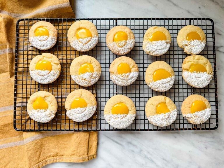 Lemon curd thumbprint cookies are on a wire cooling rack and have been dusted with confectioners' sugar.