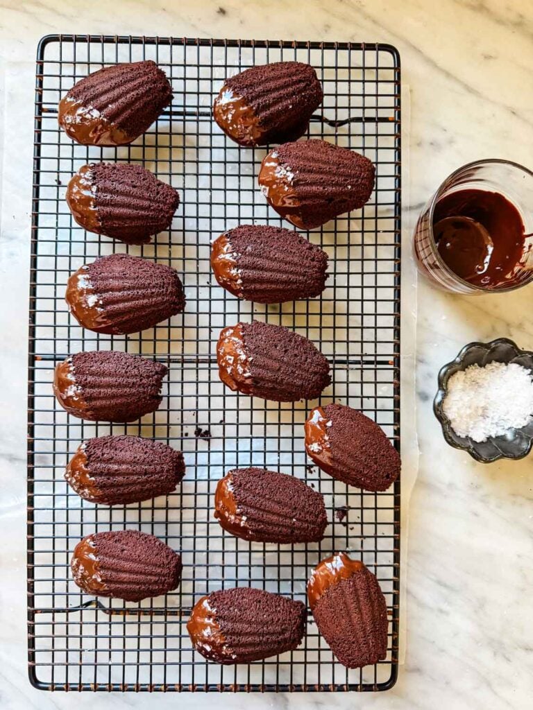 Madeleine cakes have been dipped in chocolate and are cooling on a wire rack.