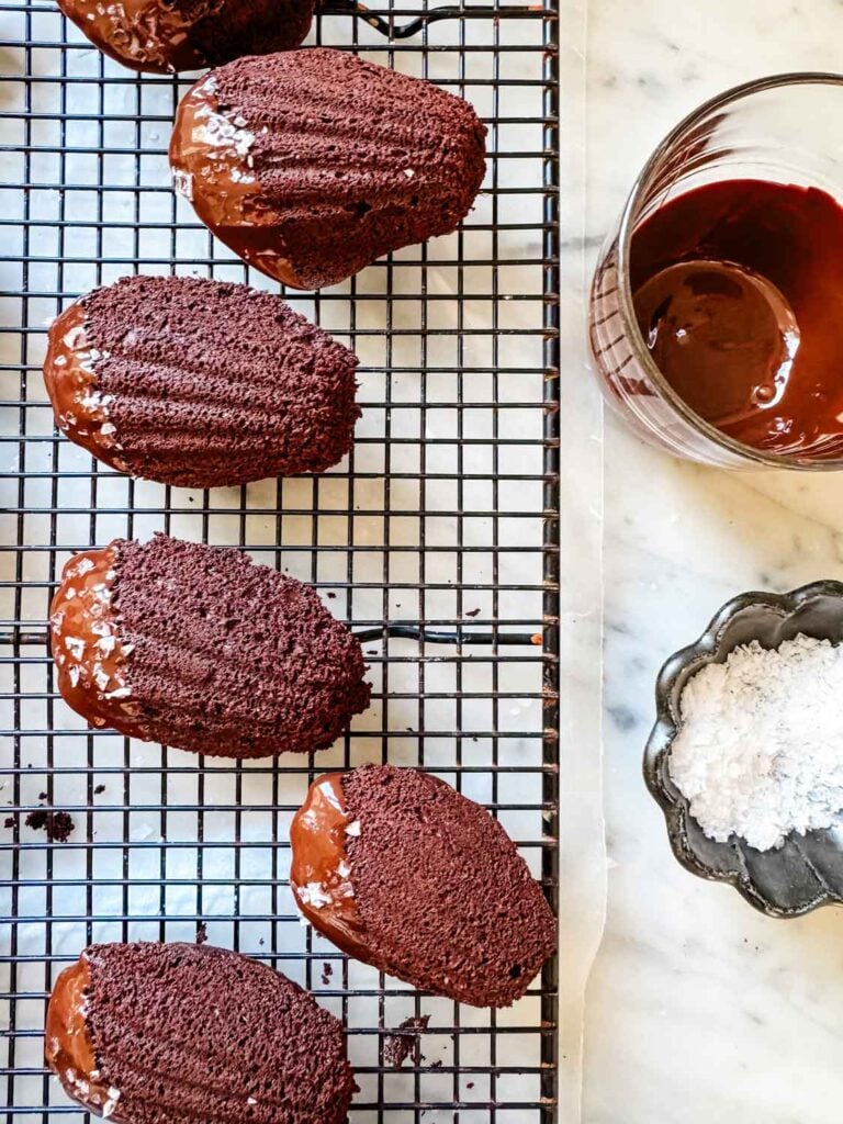 Sea salt has been sprinkled on the dipped end of Madeleine cakes. The chocolate is setting as they rest on a wire rack.