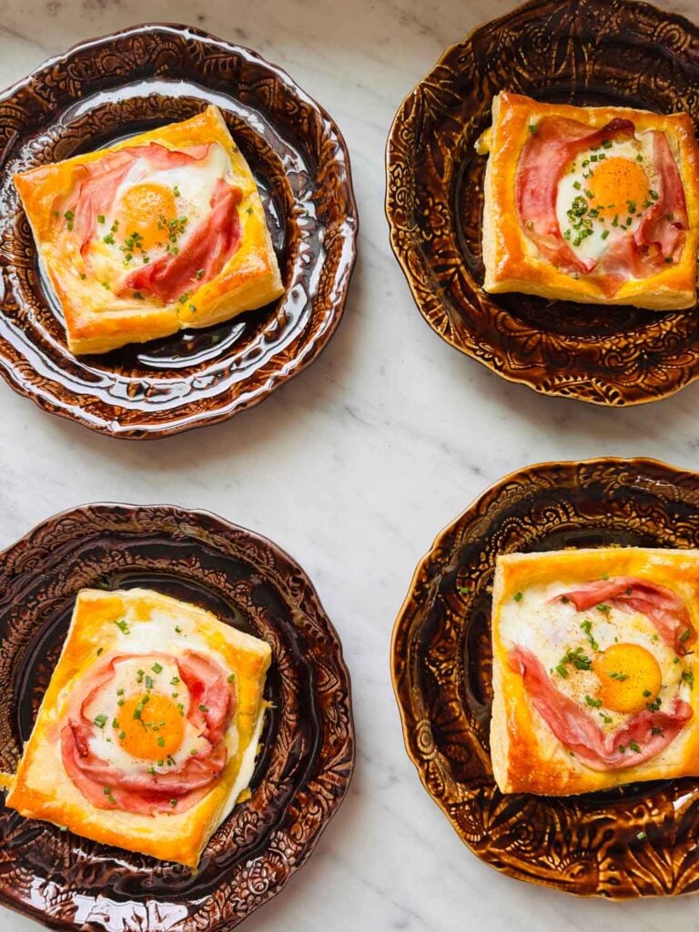 Flaky puff pastry croque madame is served on small brown plates.