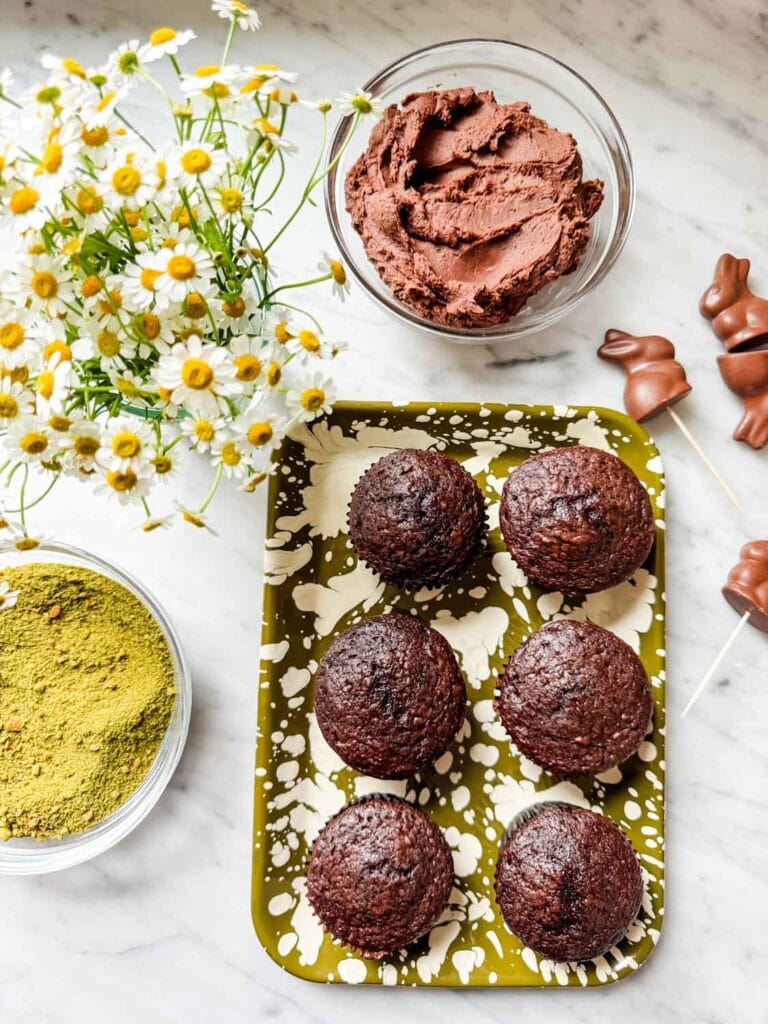 Chocolate cupcakes with matcha moss, chocolate bunnies on green splatter tray. Chamomile flowers.