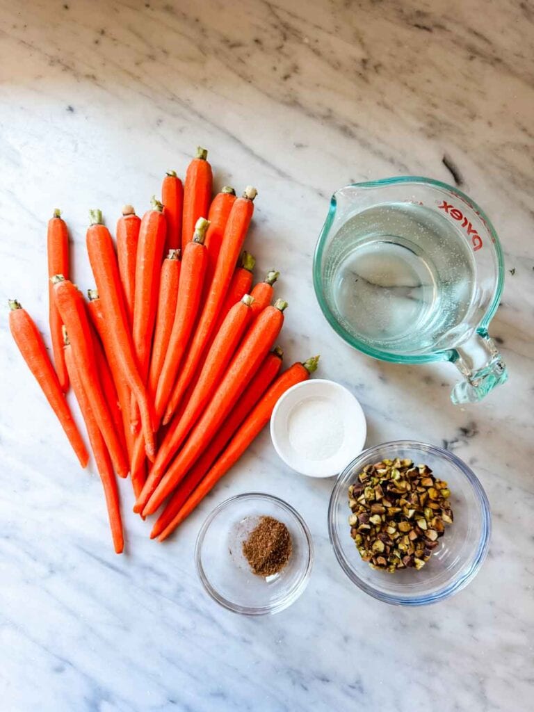 Peeled carrots on marble countertop, measuring cup of water, small dishes.