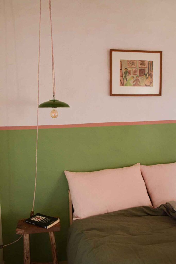 Painted green half wall with a pink stripe above in a bedroom.