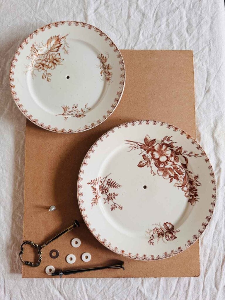 Two sizes of brown and white plates with holes in center, and hardware for tiered stand on board with washers.