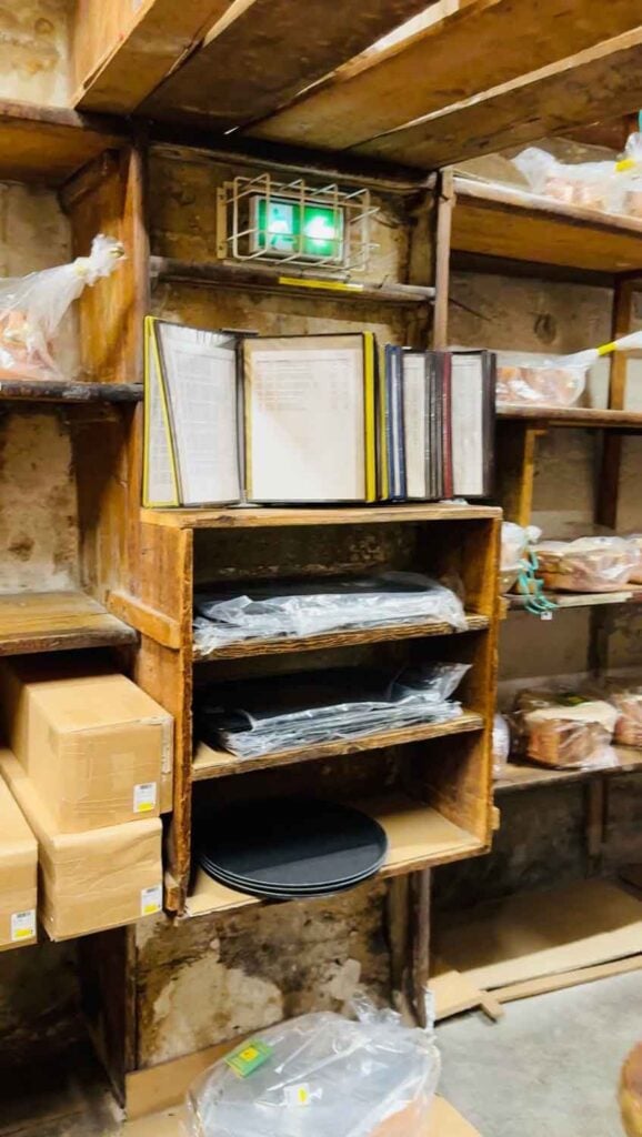 Price books, with plastic sleeves, are mixed among the wooden shelves of products in the basement of E. Dehillerin in Paris.
